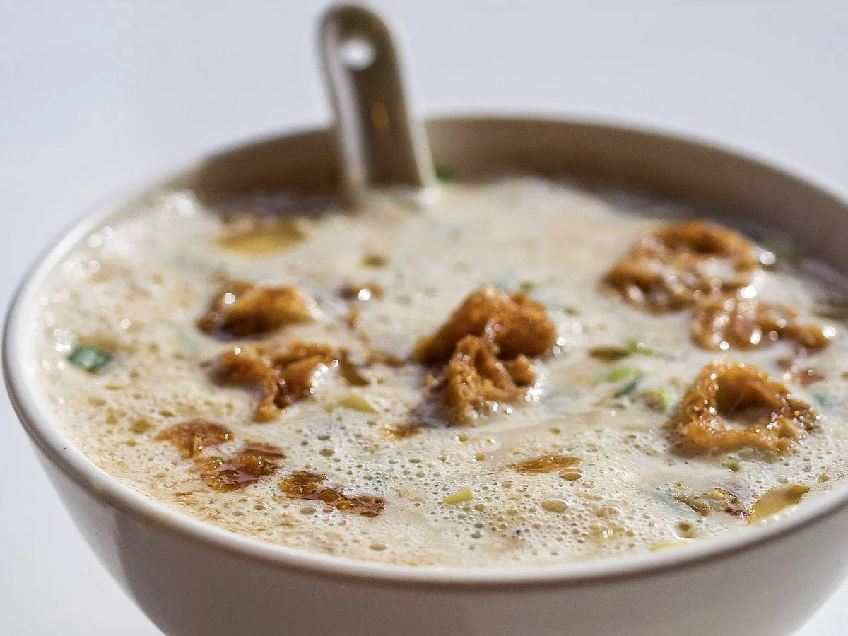 Bowl of savory soy milk with fried youtiao pieces and a spoon