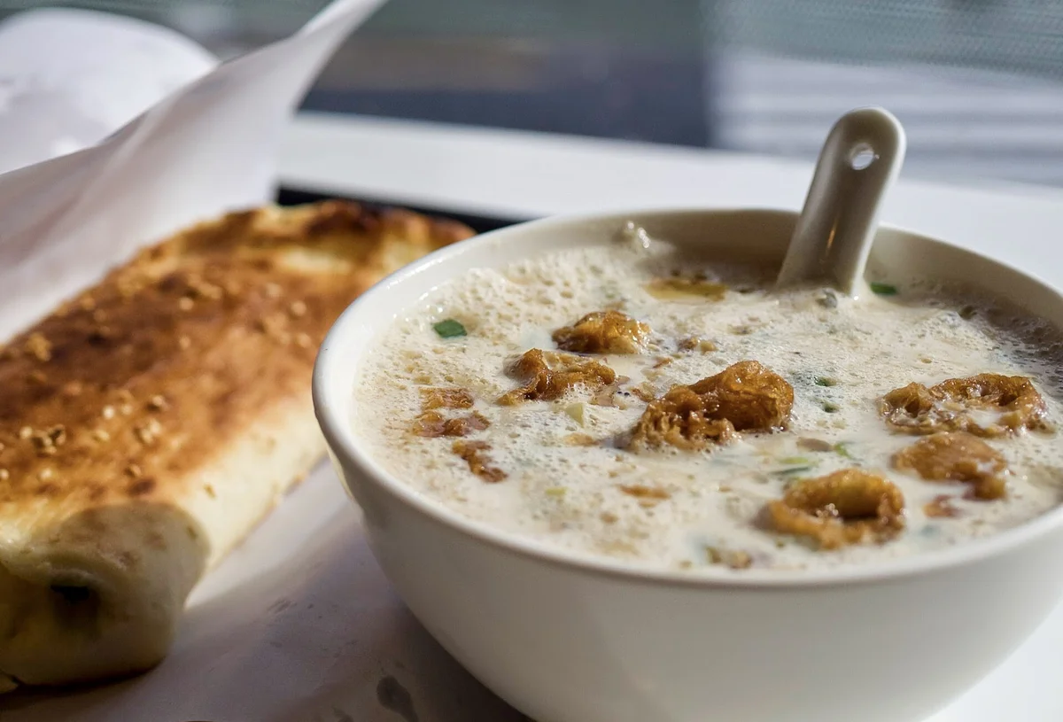 Savory soy milk bowl with youtiao pieces and flatbread on a breakfast tray