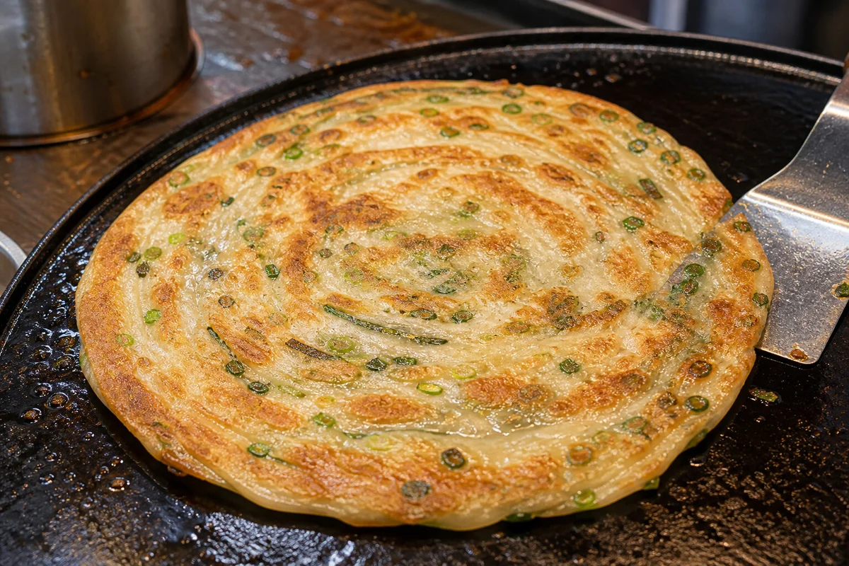 Shanghai scallion pancake cooking on a hot griddle with crisp browned surface