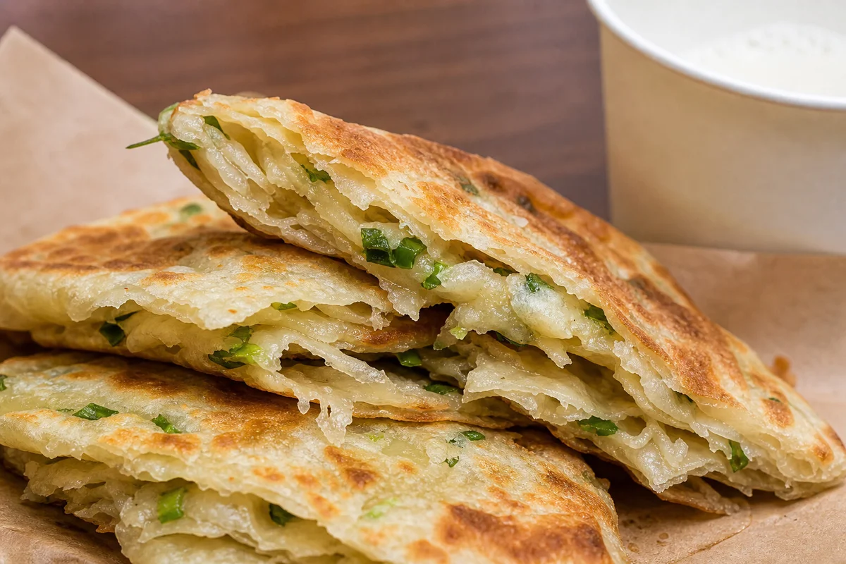 Torn Shanghai scallion pancake showing flaky layers and green scallions inside