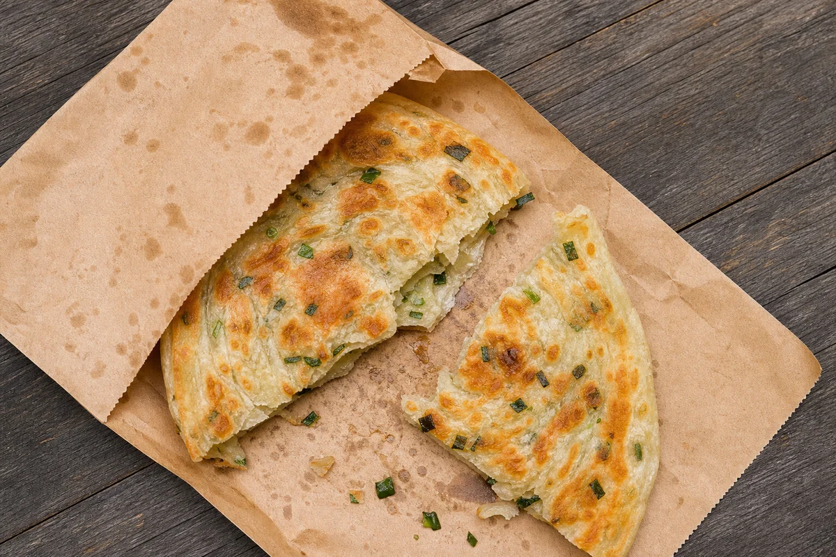 Shanghai scallion pancake pieces served in a paper sleeve with crisp golden layers