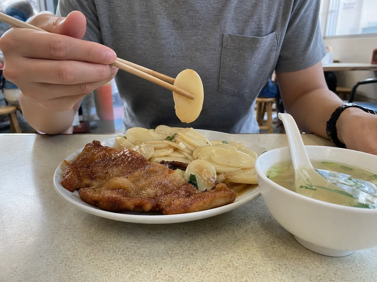Diner lifting an oval nian gao slice from a Shanghai paigu niangao plate with pork chop and clear soup