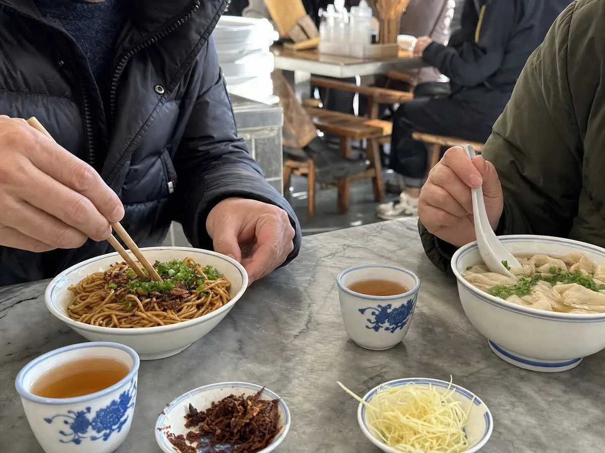 Two diners sharing scallion oil noodles and wonton soup at a Shanghai breakfast table