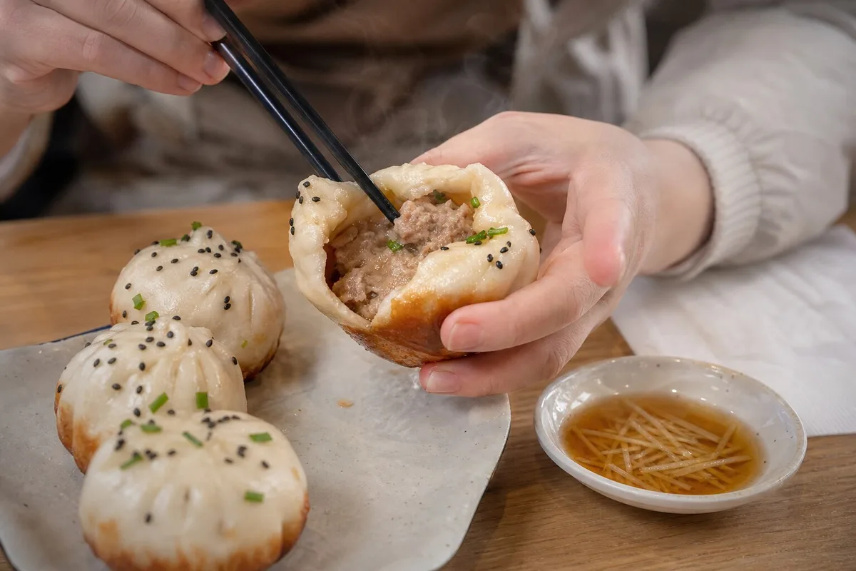 Shanghai shengjianbao opened with chopsticks to show hot pork filling and a crisp browned bottom