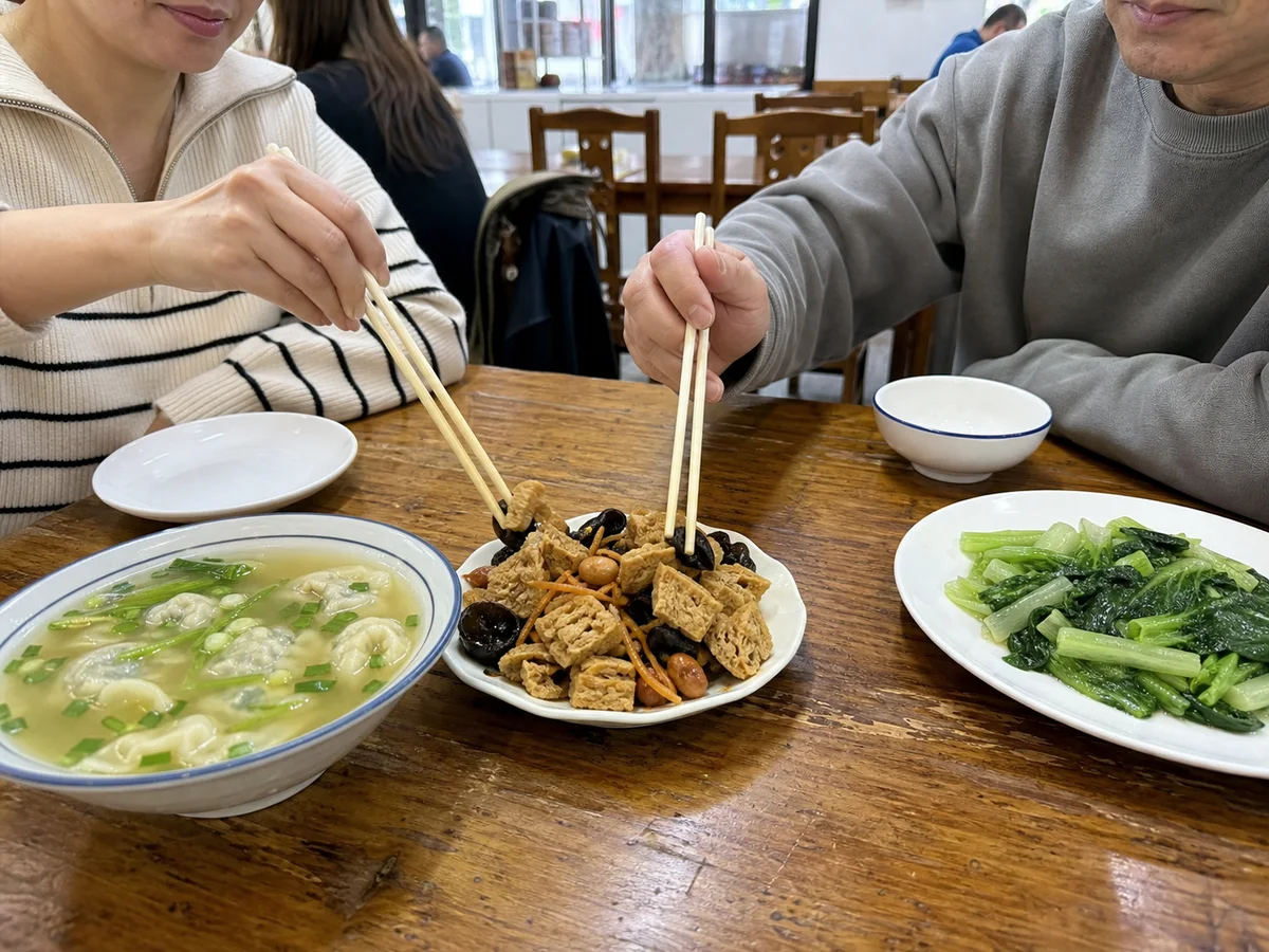 Diners sharing Shanghai kaofu with wonton soup and leafy greens at a neighborhood restaurant