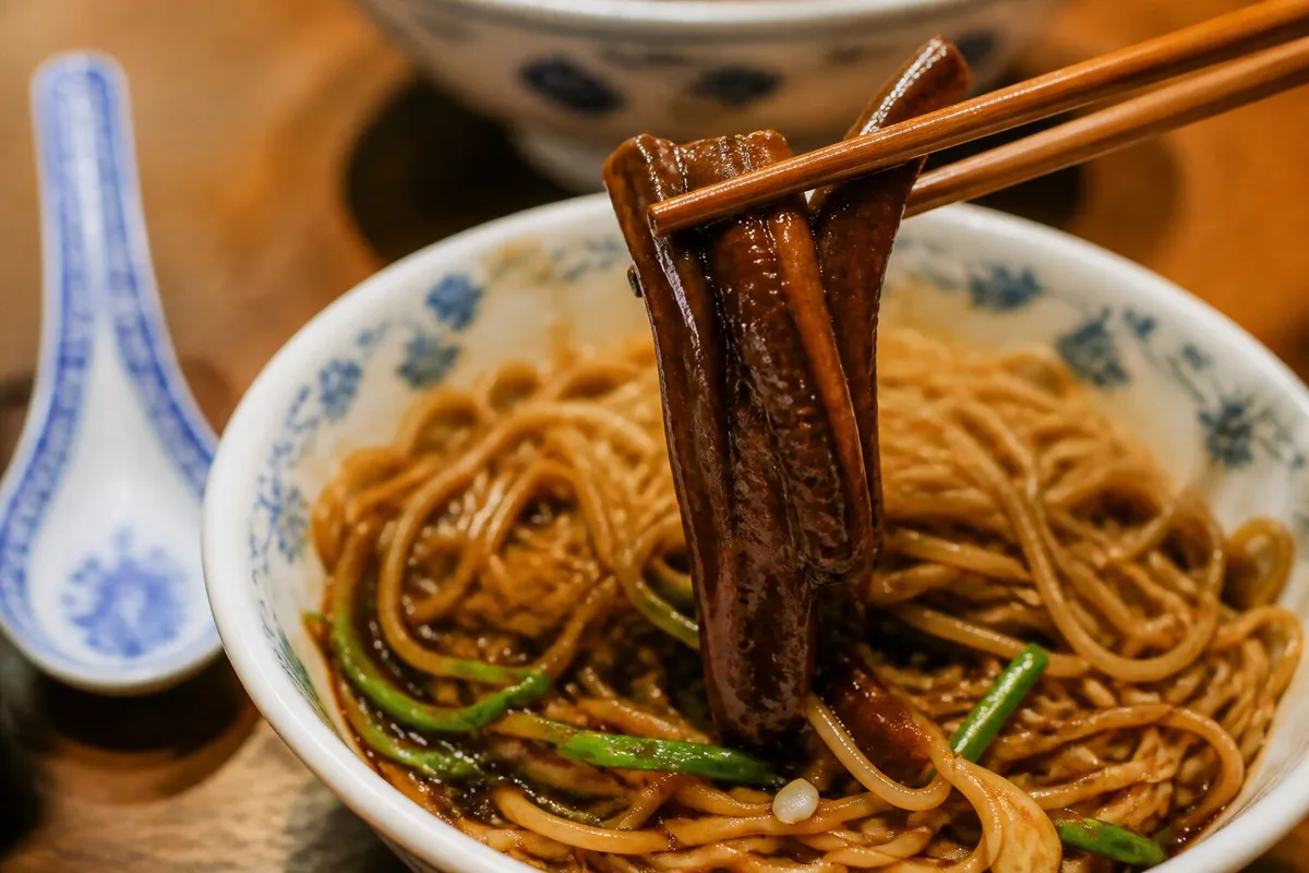 Chopsticks lifting tender eel strips over Shanghai eel noodles